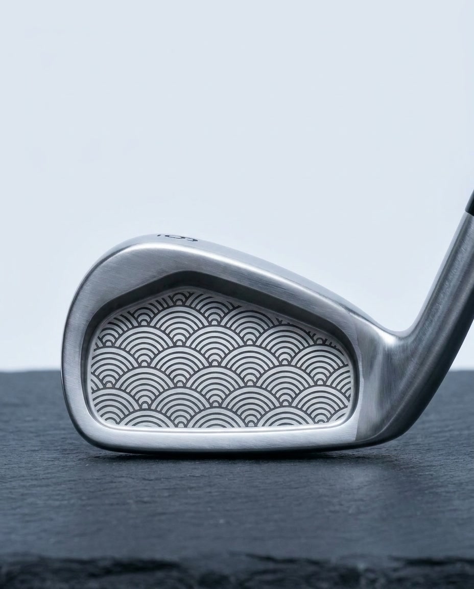 Premium golf iron cavity back laser black-annealed with a repeating Japanese seigaiha wave pattern in fine line-art, brushed satin steel on dark slate in cool studio light