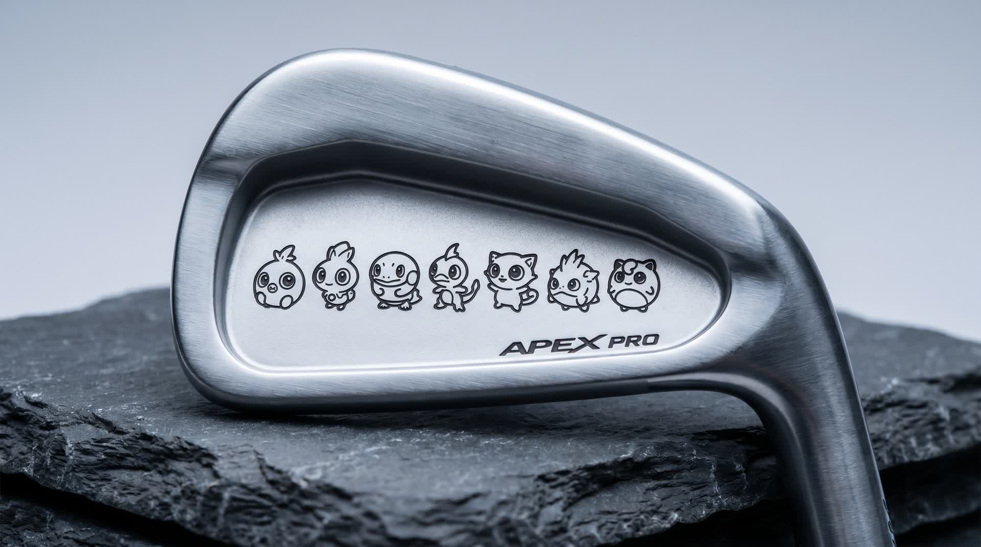 Macro of a premium golf iron cavity laser black-annealed with a row of small cartoon creature characters in clean line-art, flat dark marks on brushed satin steel, shot on dark slate in cool studio light
